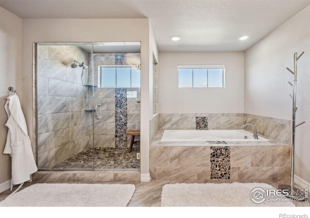 full bath with a stall shower, a garden tub, a textured ceiling, and baseboards