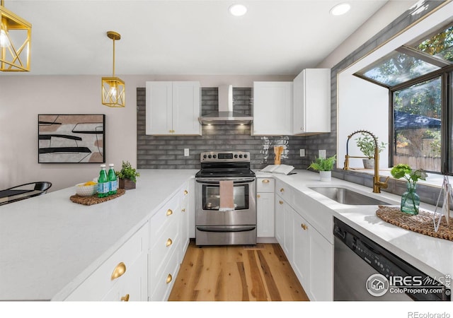 kitchen with stainless steel appliances, white cabinets, wall chimney range hood, and sink