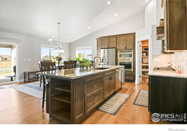 kitchen featuring lofted ceiling, a kitchen island with sink, sink, light stone countertops, and appliances with stainless steel finishes