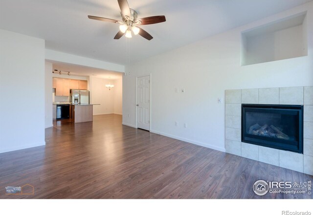 unfurnished living room with ceiling fan, a tiled fireplace, and dark wood-type flooring