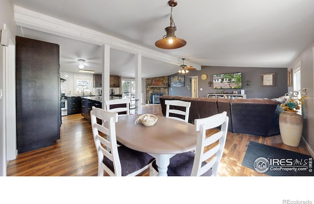 dining room with a ceiling fan, lofted ceiling, a stone fireplace, and wood finished floors