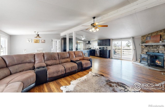 living area featuring a ceiling fan, a stone fireplace, lofted ceiling with beams, and wood finished floors