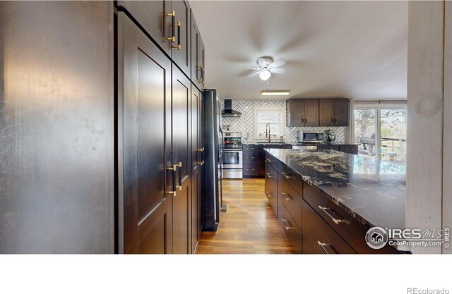 kitchen with stainless steel appliances, decorative backsplash, light wood-style floors, a sink, and wall chimney exhaust hood