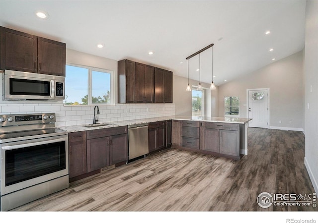 kitchen with light hardwood / wood-style floors, kitchen peninsula, pendant lighting, stainless steel appliances, and sink