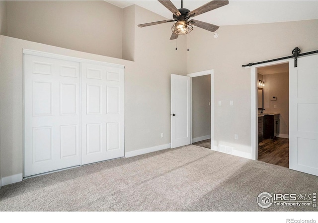 unfurnished bedroom featuring a closet, carpet, ceiling fan, and a barn door