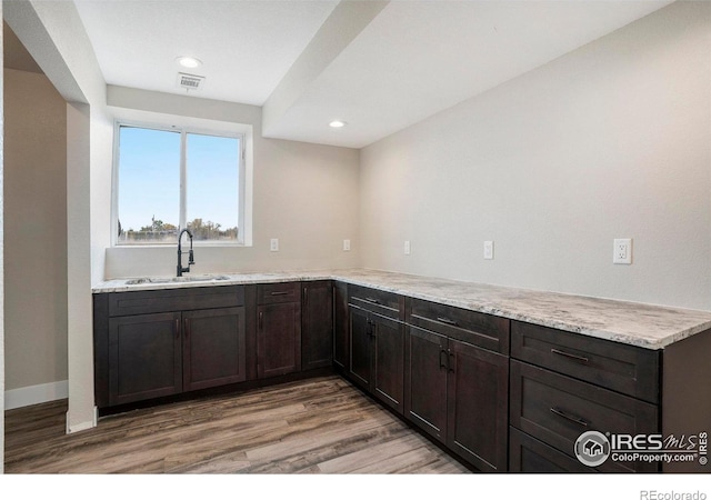 kitchen featuring dark brown cabinets, light wood-type flooring, sink, kitchen peninsula, and light stone countertops