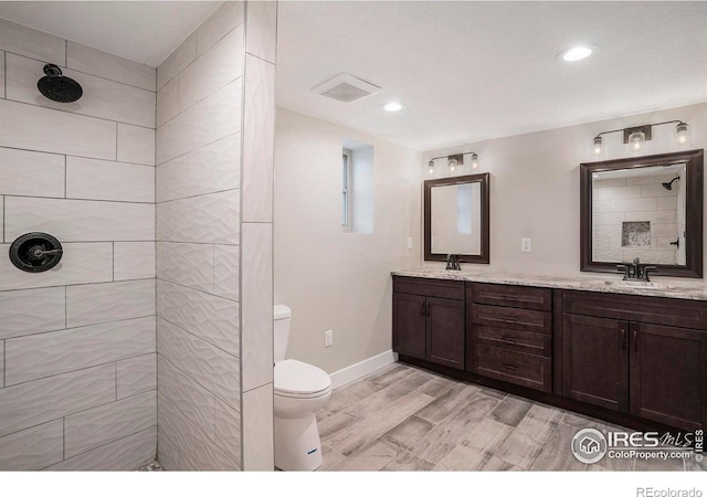 bathroom with wood-type flooring, vanity, toilet, and tiled shower