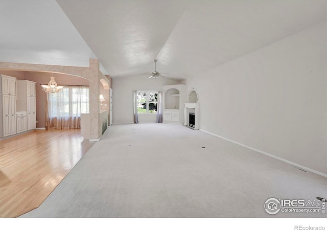 unfurnished living room featuring lofted ceiling, a healthy amount of sunlight, ceiling fan with notable chandelier, and light colored carpet