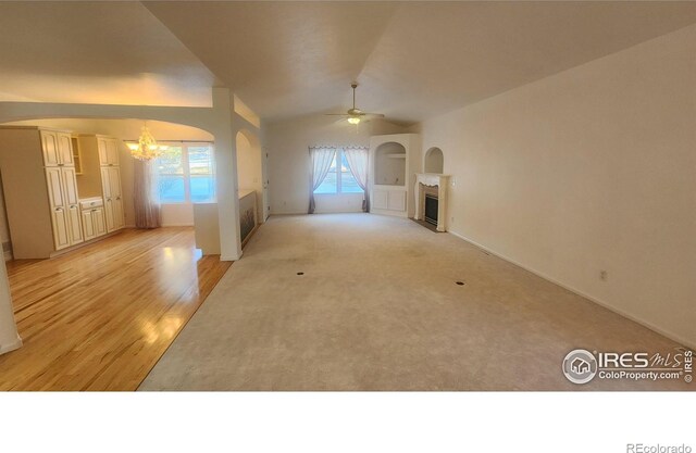 unfurnished living room with lofted ceiling, ceiling fan with notable chandelier, and light carpet