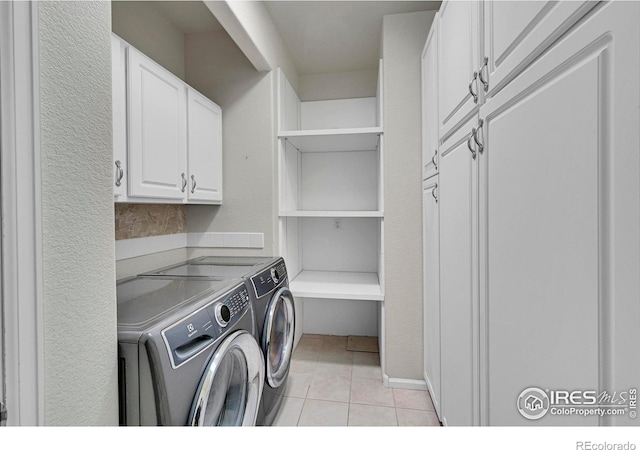 clothes washing area with cabinets, washing machine and clothes dryer, and light tile patterned flooring