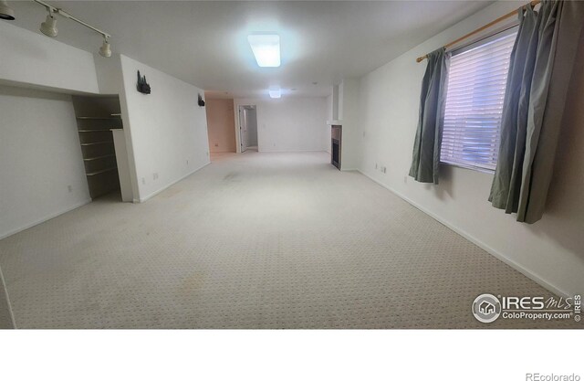 basement featuring rail lighting and light colored carpet