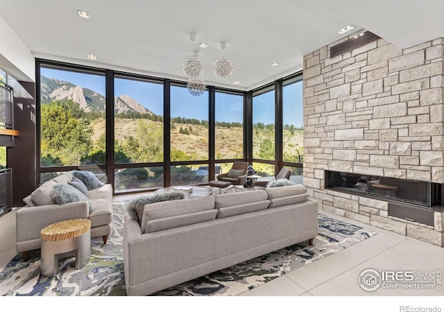 living room with a stone fireplace, a wall of windows, a healthy amount of sunlight, and tile patterned floors