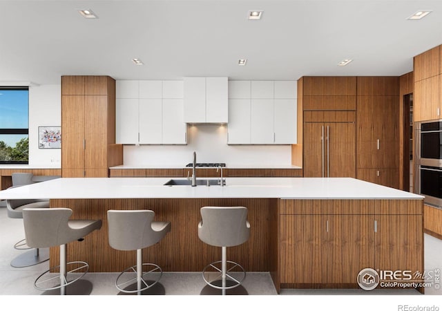 kitchen featuring sink, stainless steel double oven, a large island, white cabinetry, and paneled built in refrigerator