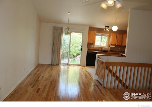 kitchen with black dishwasher, sink, hanging light fixtures, and light wood-type flooring