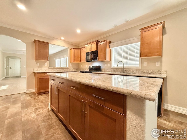 kitchen featuring light stone countertops, black appliances, light hardwood / wood-style floors, crown molding, and a center island