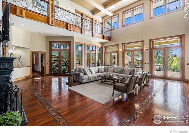 living room featuring beamed ceiling, french doors, coffered ceiling, a towering ceiling, and hardwood / wood-style floors