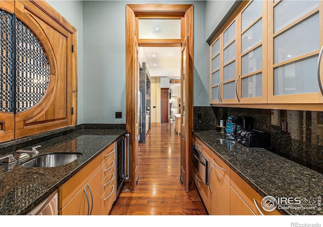 kitchen with dark stone counters, dark wood-type flooring, sink, tasteful backsplash, and beverage cooler