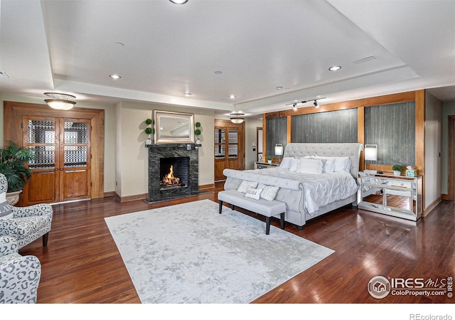 bedroom with a raised ceiling, dark wood-type flooring, and a high end fireplace