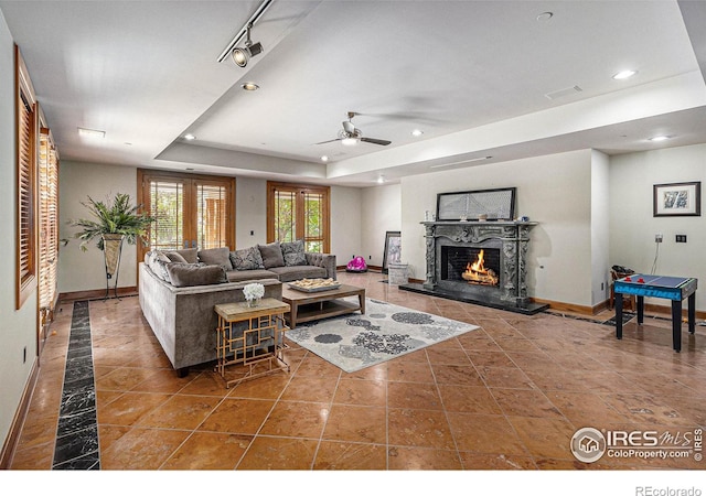 living room with a high end fireplace, ceiling fan, and a raised ceiling