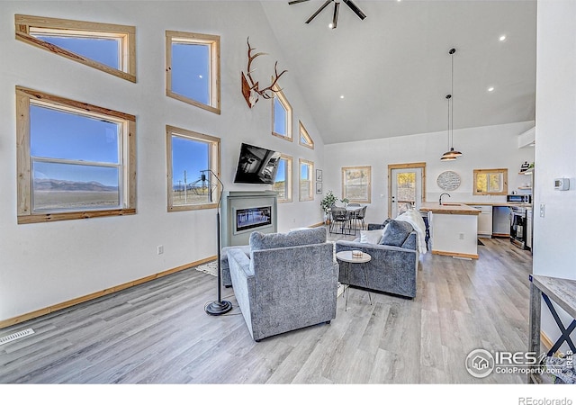 living room featuring high vaulted ceiling, light wood-type flooring, plenty of natural light, and sink