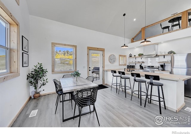 dining area with high vaulted ceiling and light wood-type flooring