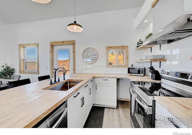 kitchen featuring white cabinets, sink, island range hood, decorative light fixtures, and appliances with stainless steel finishes