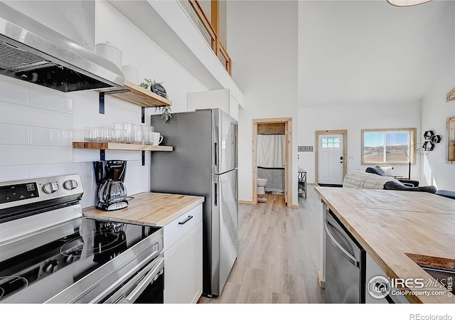 kitchen with light hardwood / wood-style floors, extractor fan, white cabinetry, appliances with stainless steel finishes, and wooden counters