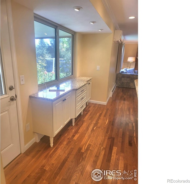 kitchen with light stone countertops, crown molding, white cabinetry, and dark hardwood / wood-style floors