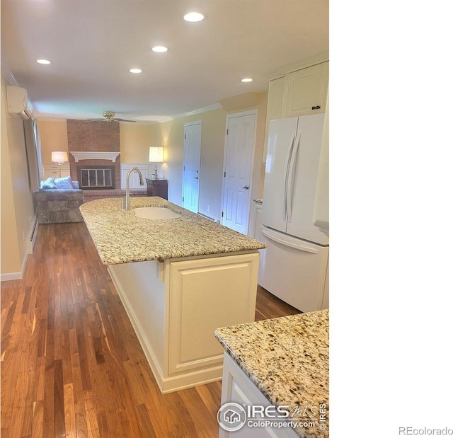 kitchen with a center island with sink, sink, light stone countertops, white refrigerator, and a fireplace