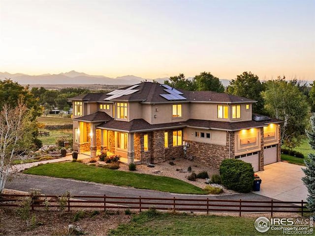 back house at dusk featuring a mountain view, a garage, and a lawn