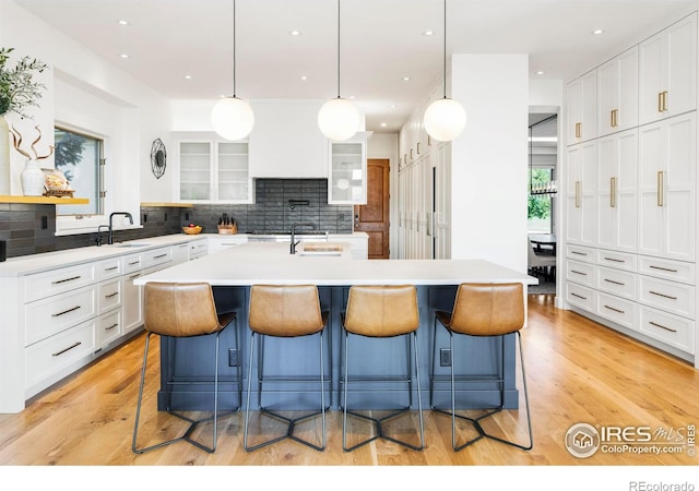 kitchen with a kitchen breakfast bar, backsplash, light hardwood / wood-style floors, and a kitchen island with sink