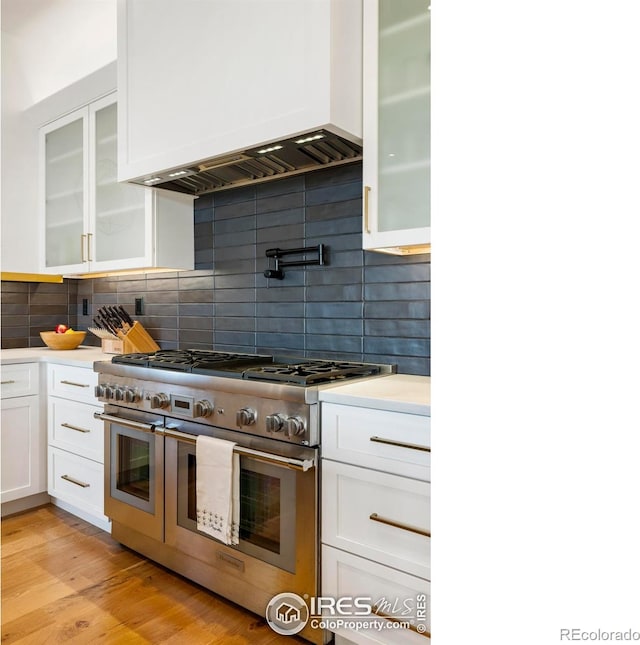 kitchen featuring light wood-type flooring, tasteful backsplash, white cabinets, range with two ovens, and premium range hood