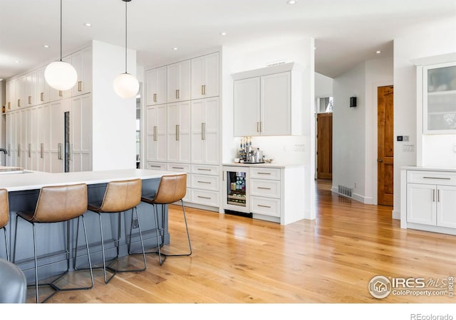 kitchen with white cabinets, wine cooler, decorative light fixtures, and light hardwood / wood-style floors