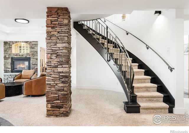 staircase with carpet floors, a stone fireplace, and decorative columns