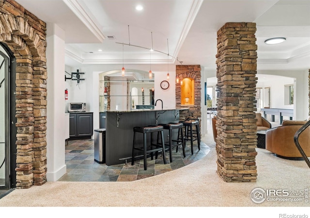 kitchen with pendant lighting, a tray ceiling, dark colored carpet, a breakfast bar, and ornate columns