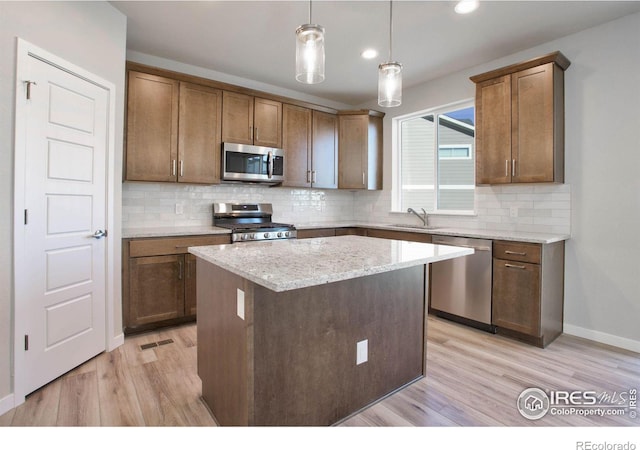 kitchen with a center island, hanging light fixtures, sink, light wood-type flooring, and appliances with stainless steel finishes