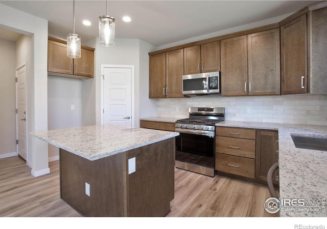 kitchen with light hardwood / wood-style floors, light stone counters, hanging light fixtures, and appliances with stainless steel finishes