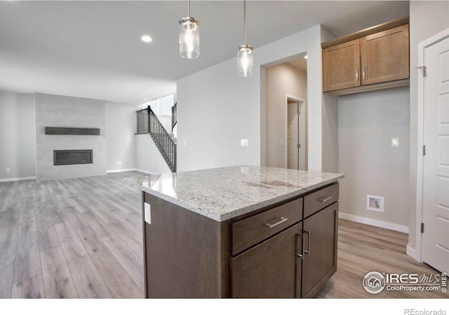 kitchen featuring light stone counters, a large fireplace, light hardwood / wood-style flooring, a center island, and hanging light fixtures