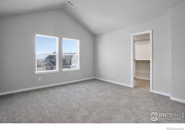 unfurnished bedroom featuring a closet, a walk in closet, light carpet, and vaulted ceiling