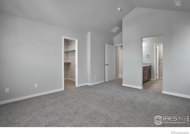 unfurnished bedroom featuring ensuite bathroom, light colored carpet, vaulted ceiling, a spacious closet, and a closet