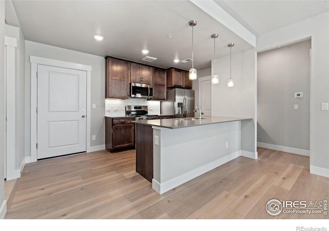 kitchen with pendant lighting, tasteful backsplash, dark brown cabinets, light hardwood / wood-style flooring, and appliances with stainless steel finishes