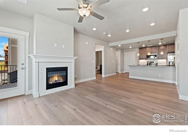 unfurnished living room with a brick fireplace, light wood-type flooring, and ceiling fan