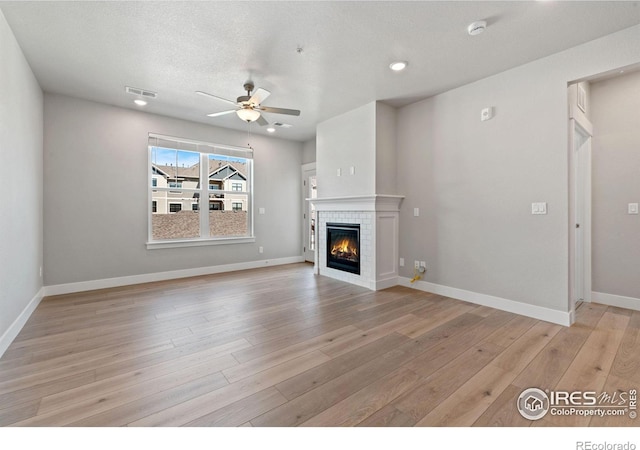 unfurnished living room with ceiling fan, a textured ceiling, a tiled fireplace, and light hardwood / wood-style floors