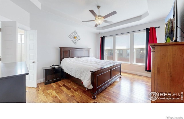 bedroom featuring a raised ceiling, baseboards, ceiling fan, and light wood finished floors