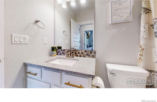 bathroom with a textured wall, vanity, and toilet