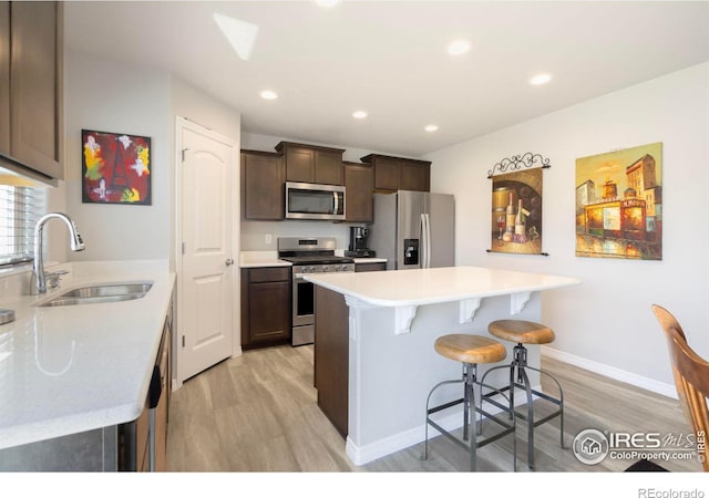 kitchen featuring stainless steel appliances, dark brown cabinetry, light wood-type flooring, and sink