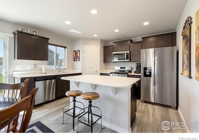 kitchen with appliances with stainless steel finishes, dark brown cabinets, a center island, light hardwood / wood-style flooring, and sink