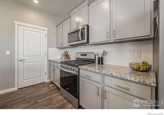 kitchen with light stone counters, gray cabinetry, dark wood-type flooring, stainless steel appliances, and decorative backsplash