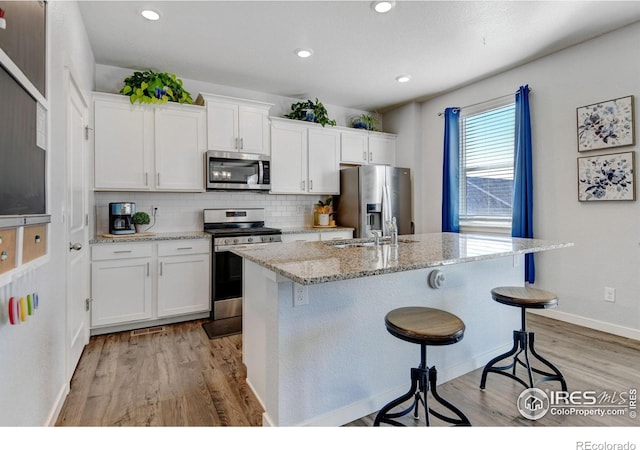 kitchen with light stone countertops, appliances with stainless steel finishes, light hardwood / wood-style floors, and white cabinetry