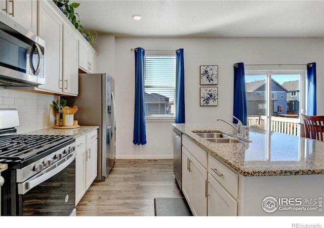 kitchen with light hardwood / wood-style floors, an island with sink, white cabinetry, stainless steel appliances, and light stone countertops